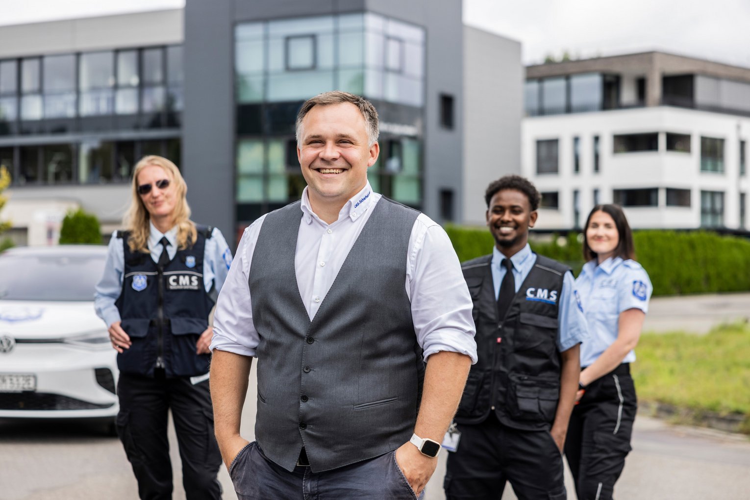 Lächelnder Sicherheitsleiter mit seinem Team von CMS-Sicherheit vor einem modernen Firmengebäude